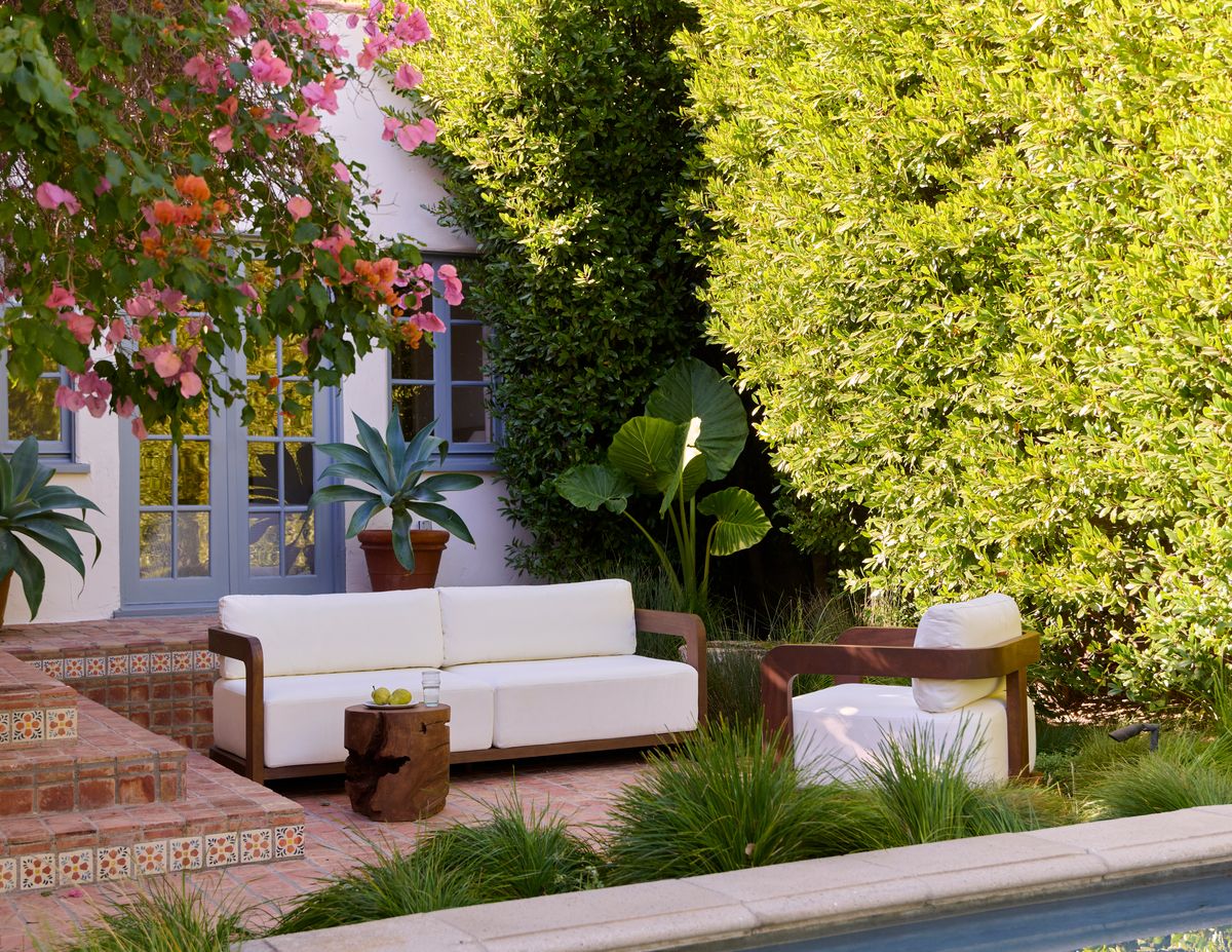 Lush tropical patio with vibrant pink flowers, white modern seating, and verdant ivy-covered walls creating a serene botanical escape.