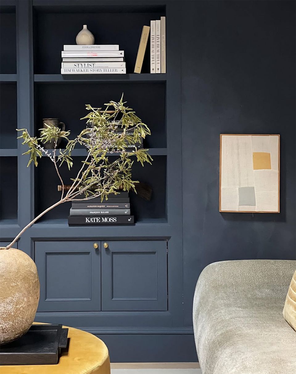 Modern eclectic shelving in deep navy with curated styling mixing natural elements, books, and warm brass accents