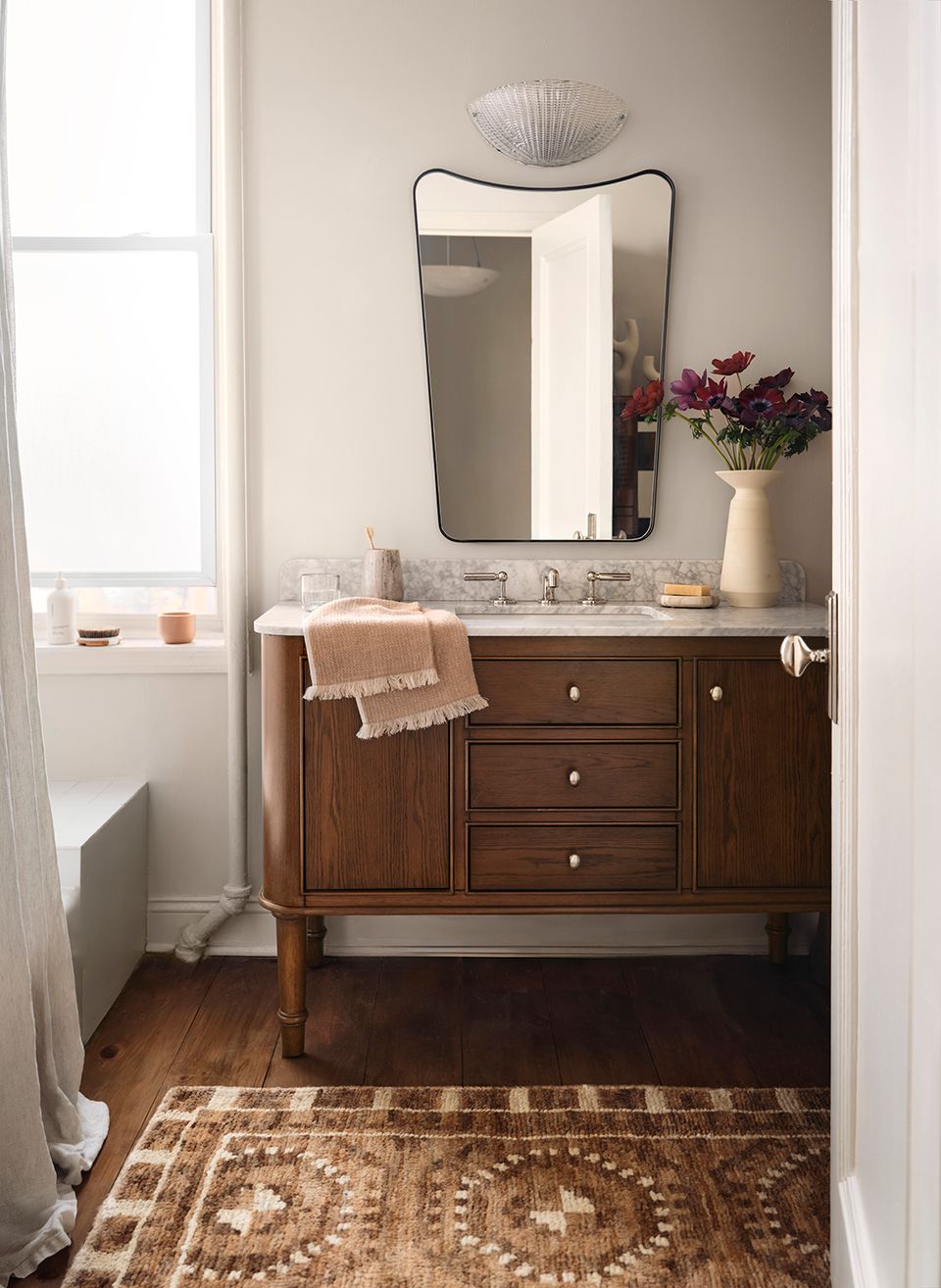 Spa-inspired bathroom with dark wood vanity, arched mirror, marble countertop, and patterned rug