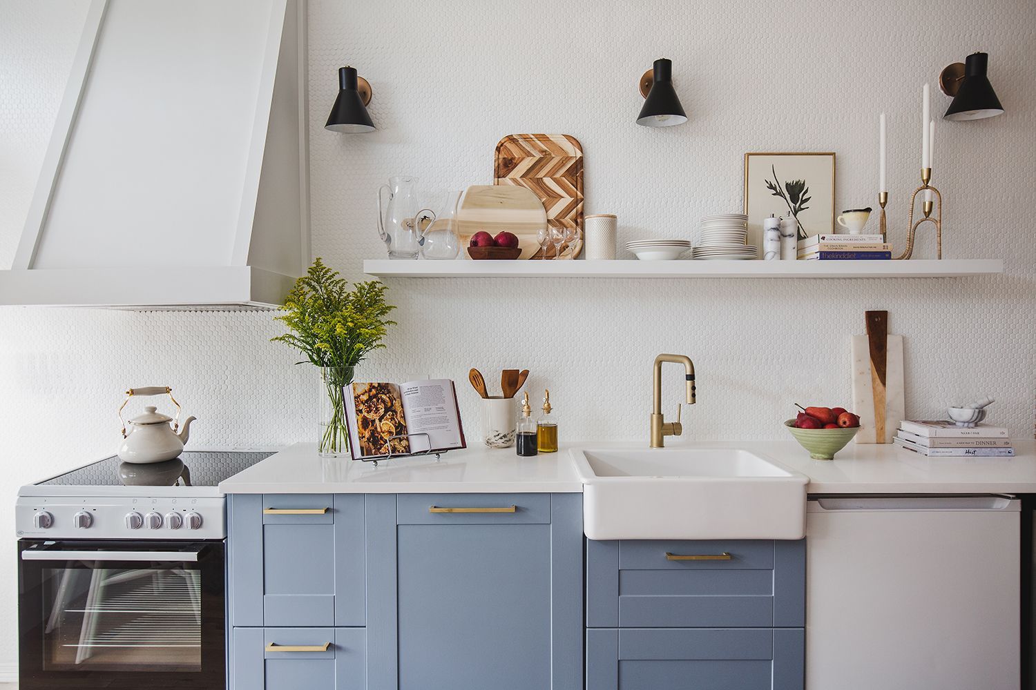 Bright all-white kitchen with blue base cabinets, natural wood accents, warm brass fixtures, and welcoming atmosphere