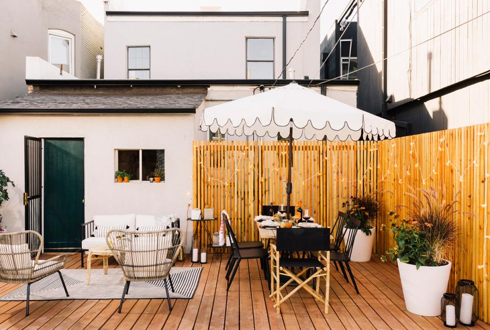 Modern patio with warm wood decking, black dining table, natural linen umbrella, and minimalist Scandinavian furnishings