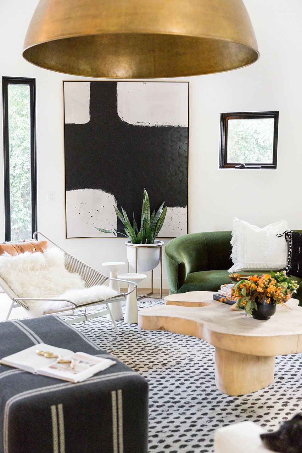 Modern living room with bold abstract wall art, jewel-tone velvet seating, brass pendant light, and geometric patterned rug