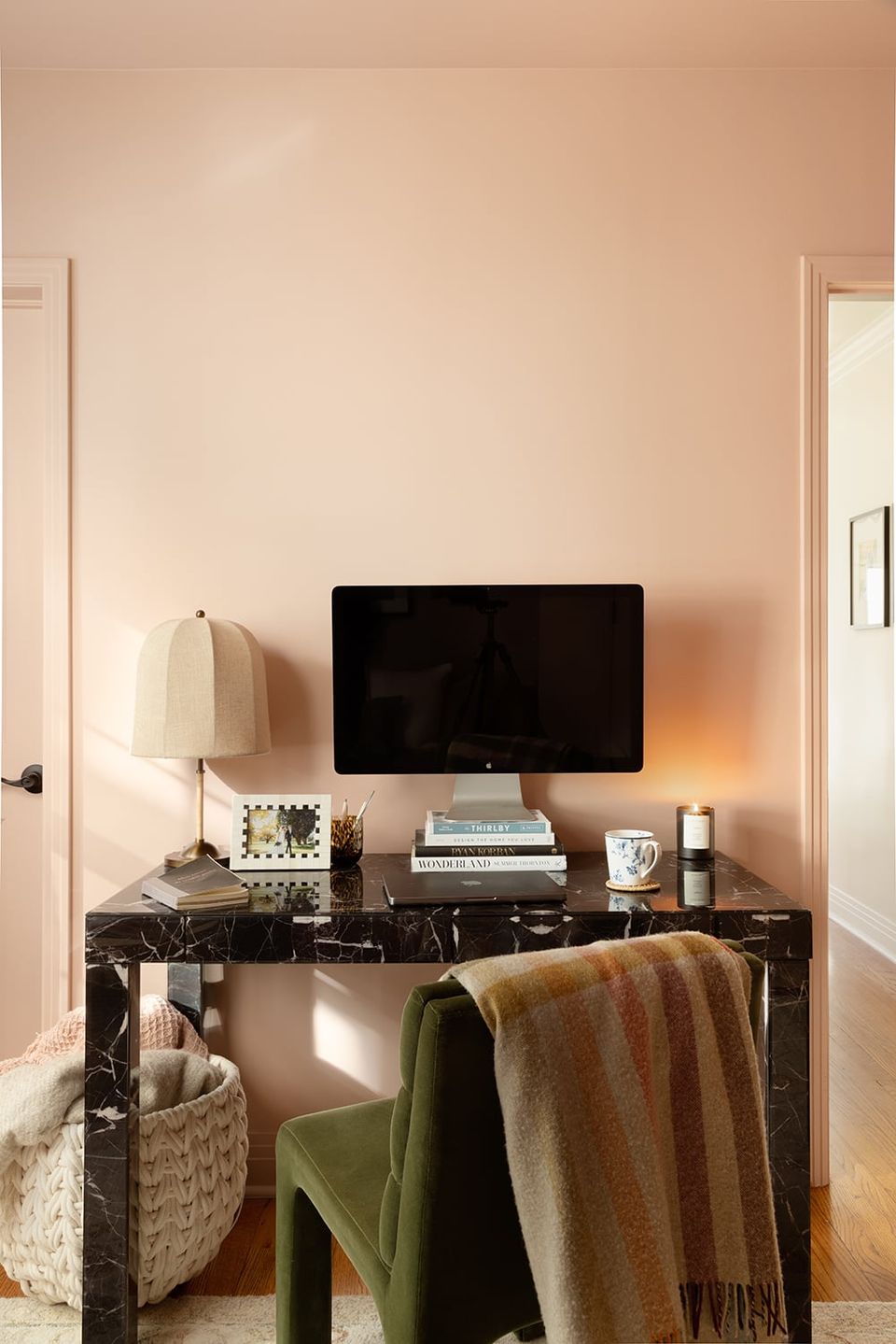 Warm, intimate office alcove with soft blush walls, black marble desk, ambient lamp lighting, and cozy layered textures