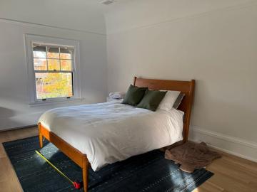 Serene mid-century bedroom with warm wood bed frame, white bedding, forest green accent pillow, and minimalist aesthetic