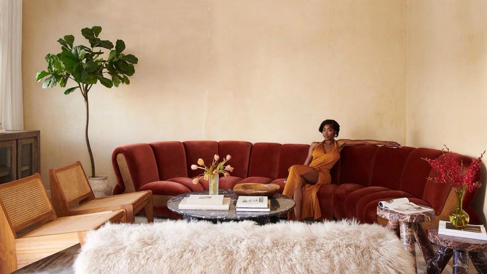 Luxe living room featuring a burgundy curved sofa, warm earth tones, and statement greenery against creamy walls