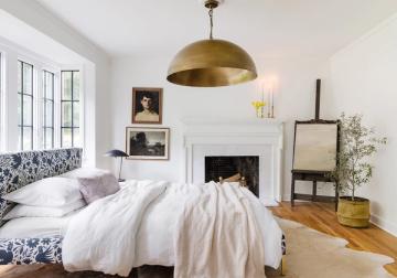Eclectic modern bedroom with white fireplace focal point, brass pendant light, patterned blue headboard, and mixed vintage-industrial style elements.