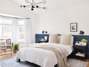 Modern organic bedroom with navy nightstands, warm wood frame, cream linens, and black geometric light fixture creating clean, nature-inspired contrast.