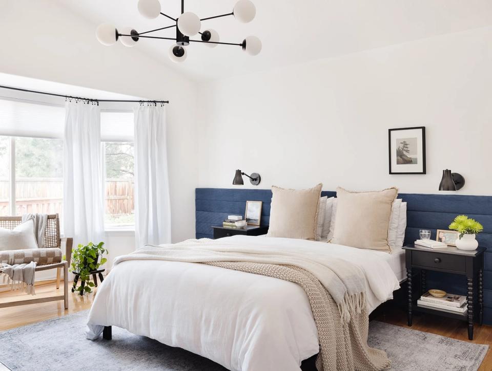 Modern organic bedroom with navy nightstands, warm wood frame, cream linens, and black geometric light fixture creating clean, nature-inspired contrast.