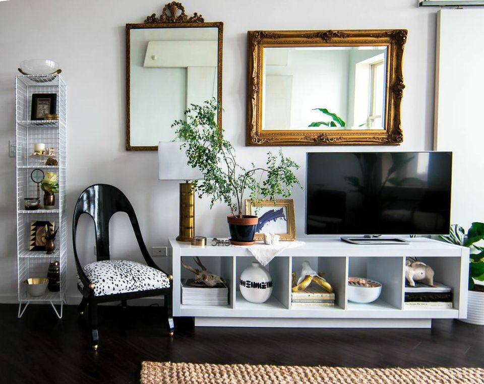 Eclectic living room with black accent chair, white media console, and vintage gold-framed mirrors against soft gray walls.