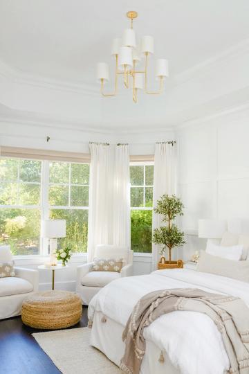 Airy modern bedroom with high ceilings, brass chandelier, white linens, and abundant natural light