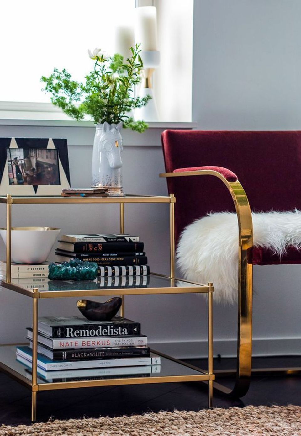 Contemporary living space pairing burgundy velvet chair with brass side table, greenery, and layered neutral textures.