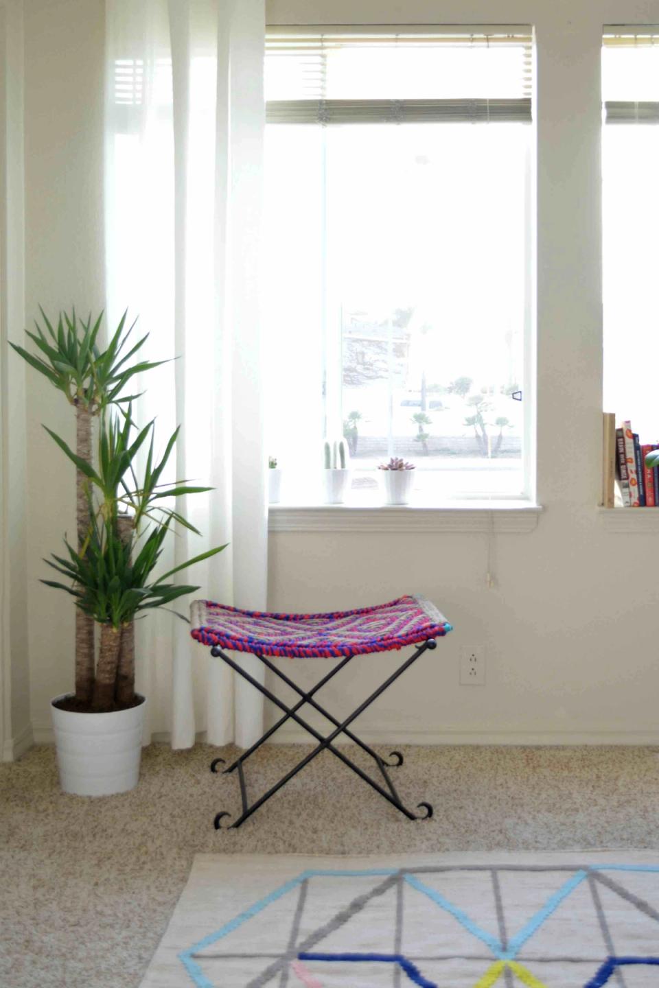 Bright coastal nook with potted palm, geometric rug, and purple woven seat near sunlit windows
