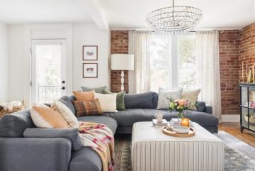 Industrial-modern living room with exposed brick, charcoal sectional, warm terracotta accents, and bright natural light