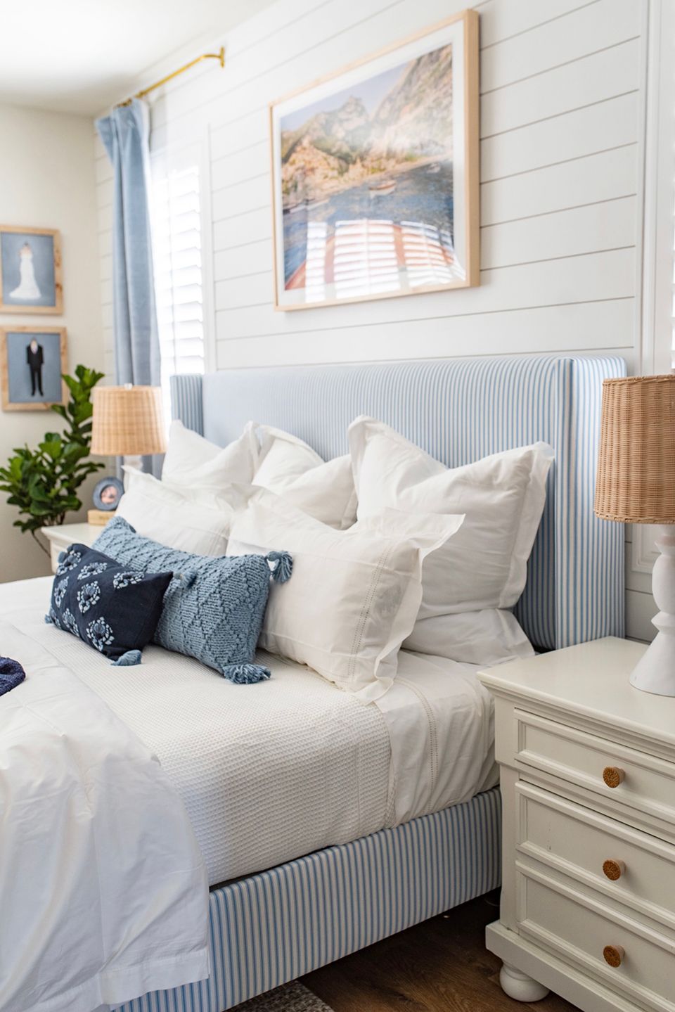 Coastal farmhouse bedroom with shiplap walls, blue striped headboard, cream linens, and brass accents