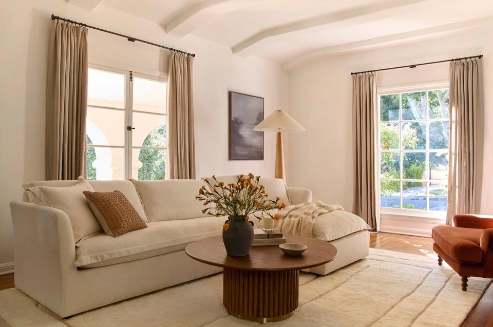 Organic modern living room with cream sofa, warm earth tones, natural wood accents, and abundant natural light from large windows
