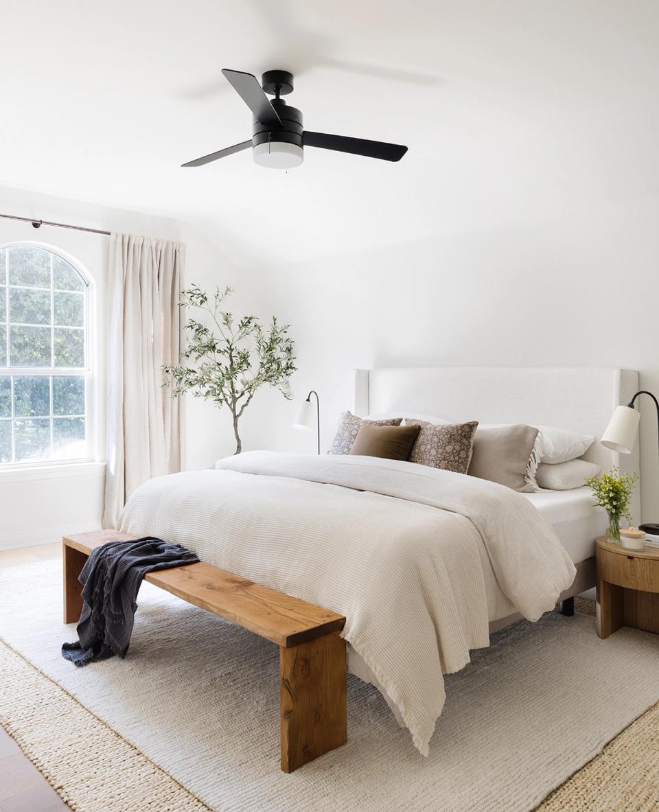 Serene minimalist bedroom with white linens, natural wood bench, potted plant, and soft neutral tones