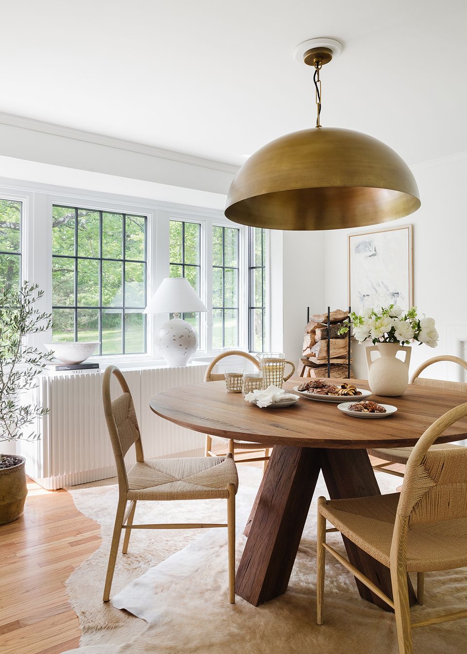 Warm mid-century modern dining space with brass pendant light, wooden round table, and natural light from grid windows