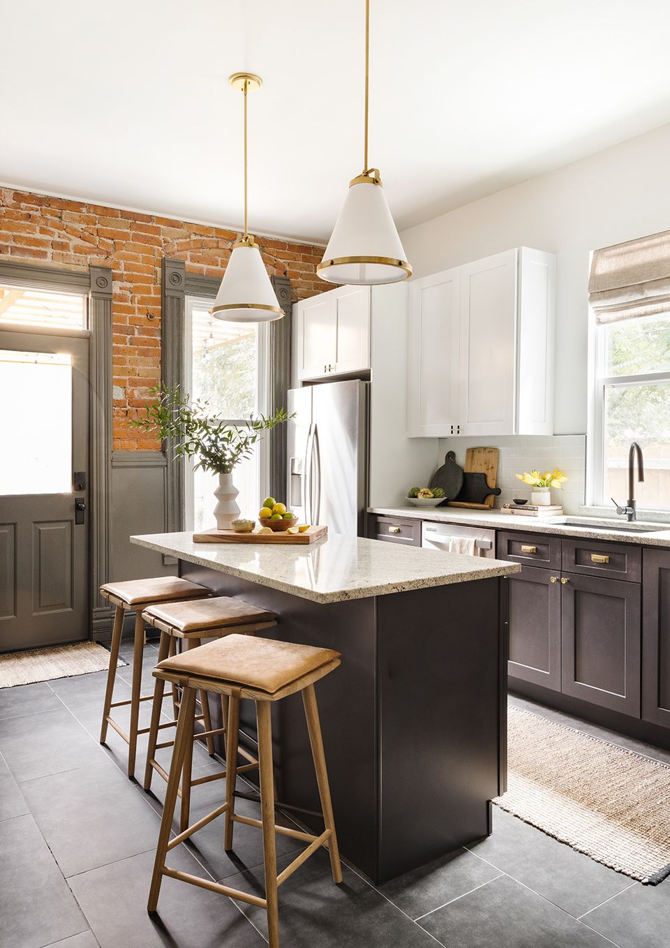 Farmhouse kitchen featuring white upper cabinets, dark charcoal island, marble top, and brick accent wall