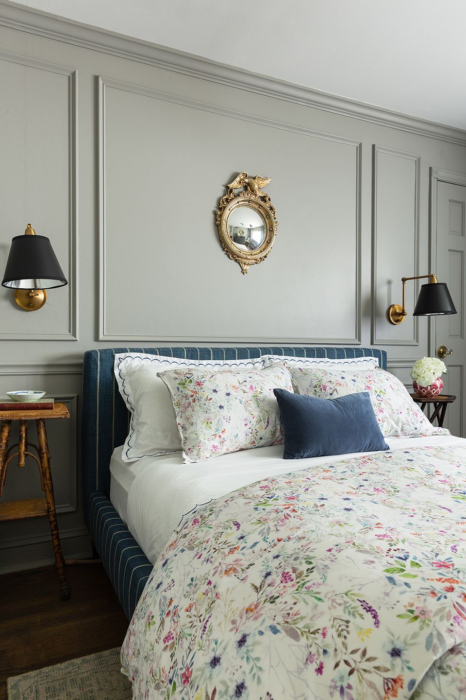 Traditional bedroom with sage green paneled walls, floral patterned bedding, and brass wall sconces