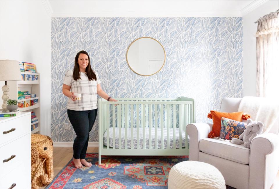 Bright nursery with soft sage crib, colorful patterned rug, and textured blue-gray wallpaper creating a whimsical, adventure-inspired space