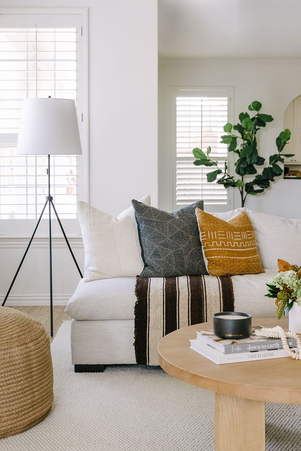 Bright living space with cream sofa, layered throw pillows in mustard and black, potted greenery, and natural wood side table showcasing warm minimalist style