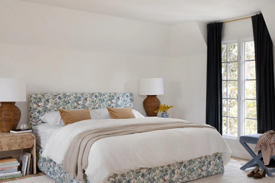 Serene bedroom with floral upholstered headboard, warm neutrals, and black curtains framing glass doors