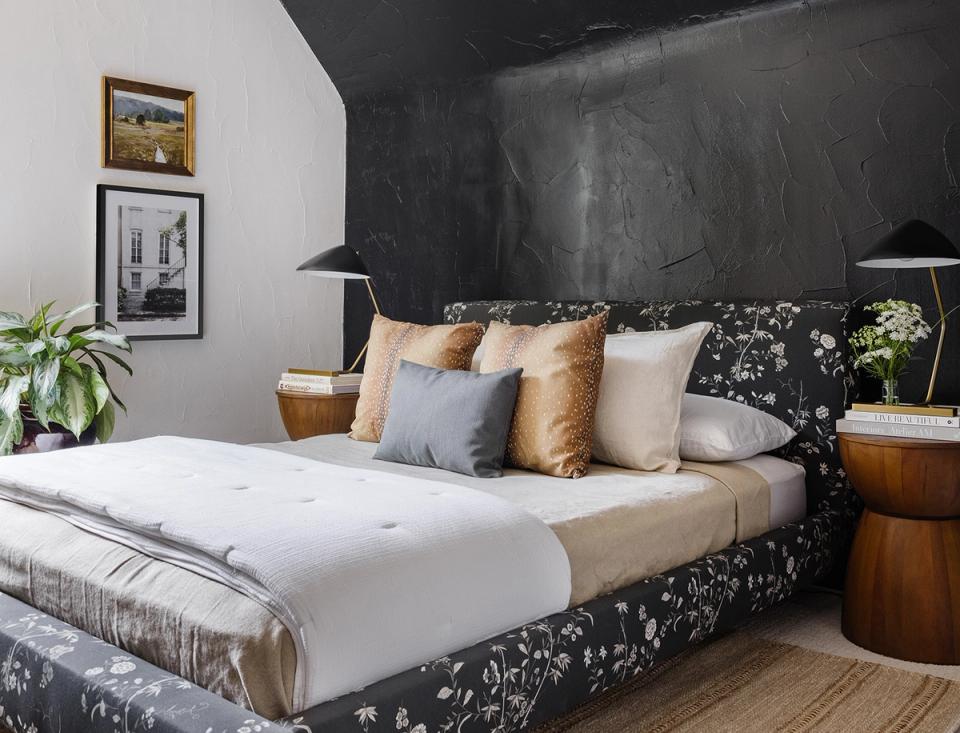Contemporary bedroom with charcoal accent wall, patterned upholstered bed, warm metallics, and layered neutral bedding