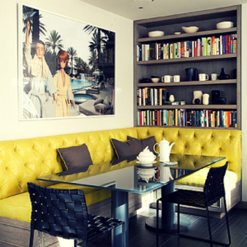 Contemporary breakfast area: yellow quilted bench seating with navy bookcase and tropical artwork