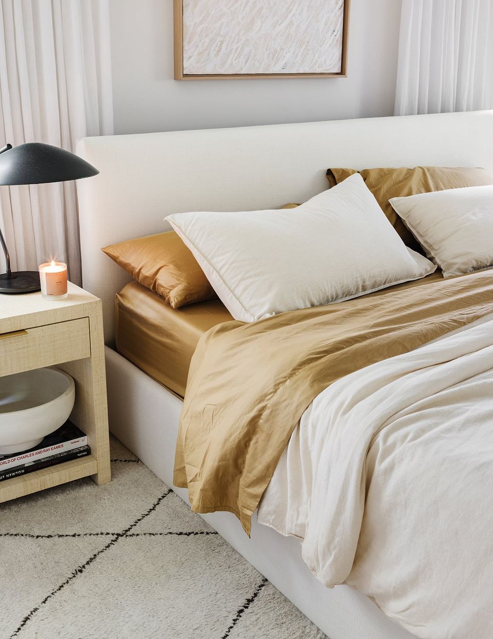 Luxe mid-century bedroom with white upholstered headboard, gold satin sheets, cream palette, and modern simplicity.