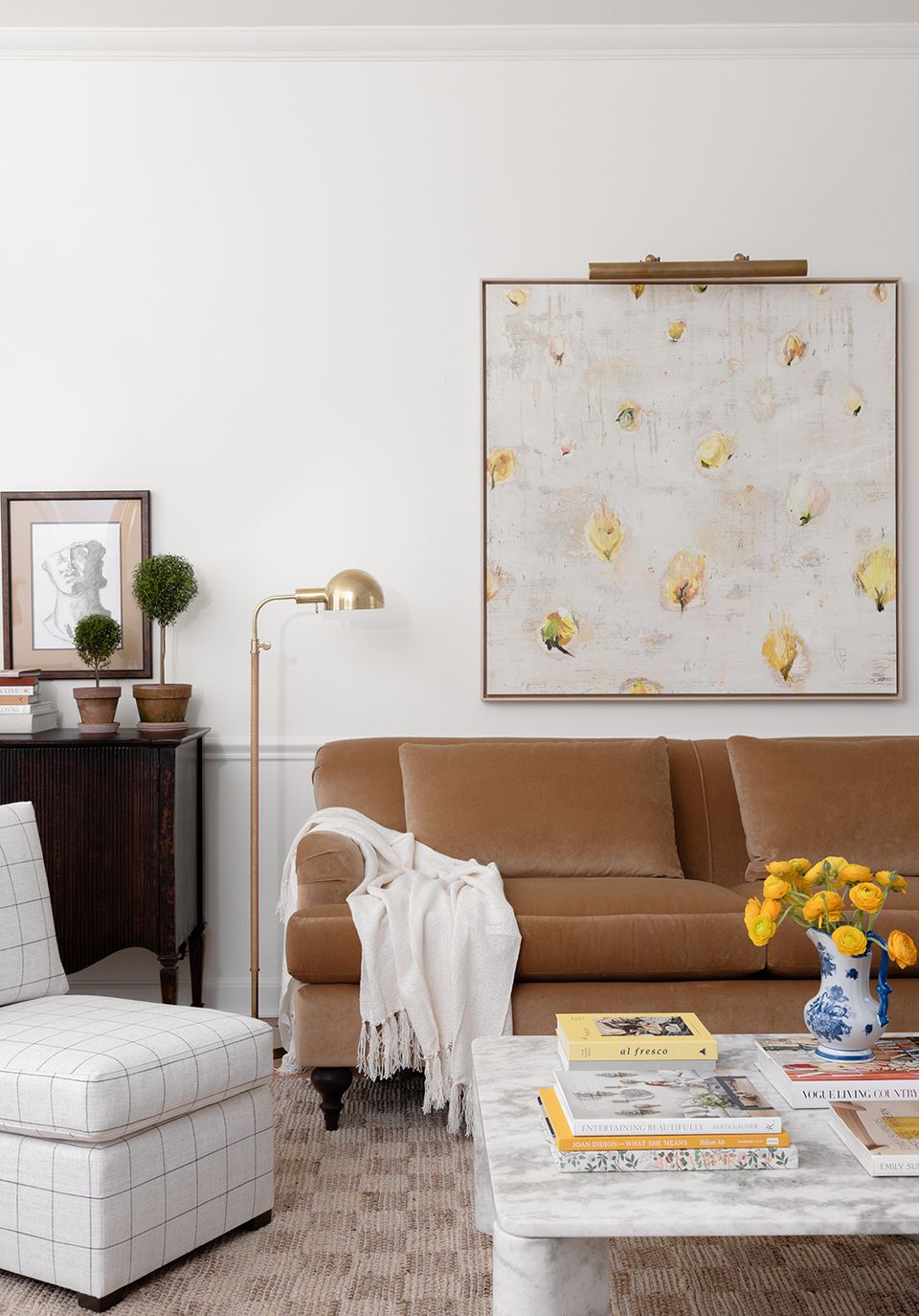 Contemporary living room with caramel sofa, white accents, and botanical artwork in warm-toned palette