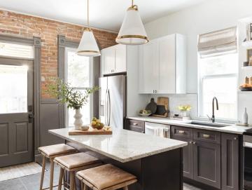 Contemporary kitchen with exposed brick, white cabinetry, marble island, and brass fixtures in warm industrial style