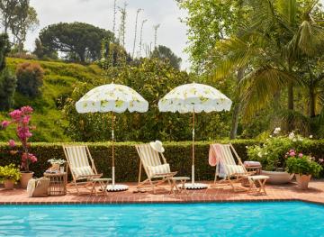 Retro 1960s poolside retreat with striped loungers, patterned umbrellas, lush landscaping