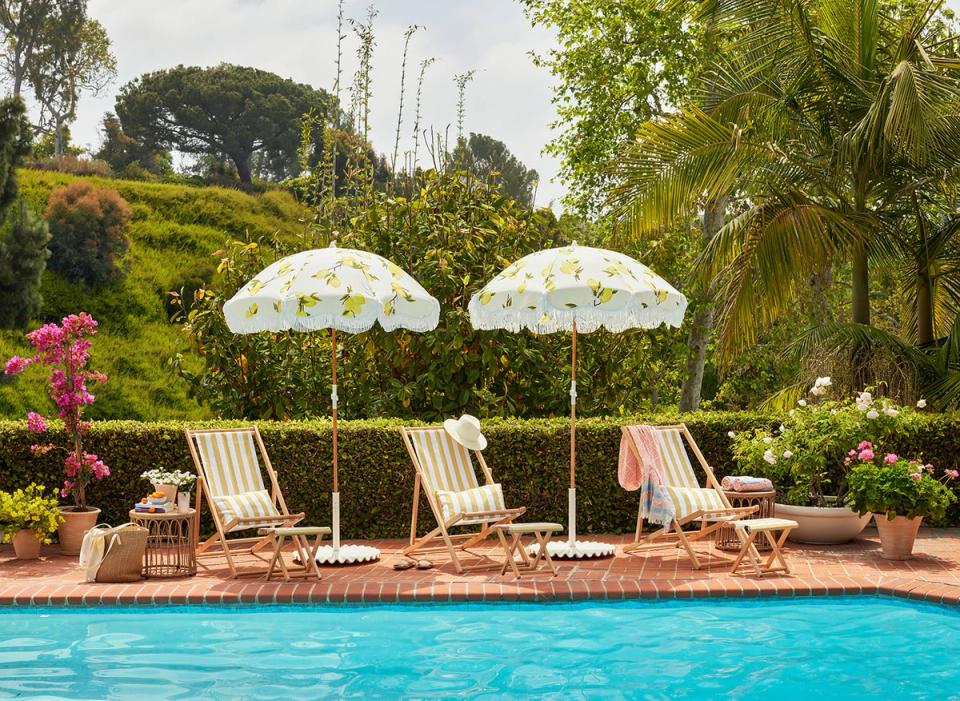 Retro 1960s poolside retreat with striped loungers, patterned umbrellas, lush landscaping