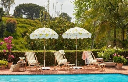 Retro 1960s poolside retreat with striped loungers, patterned umbrellas, lush landscaping