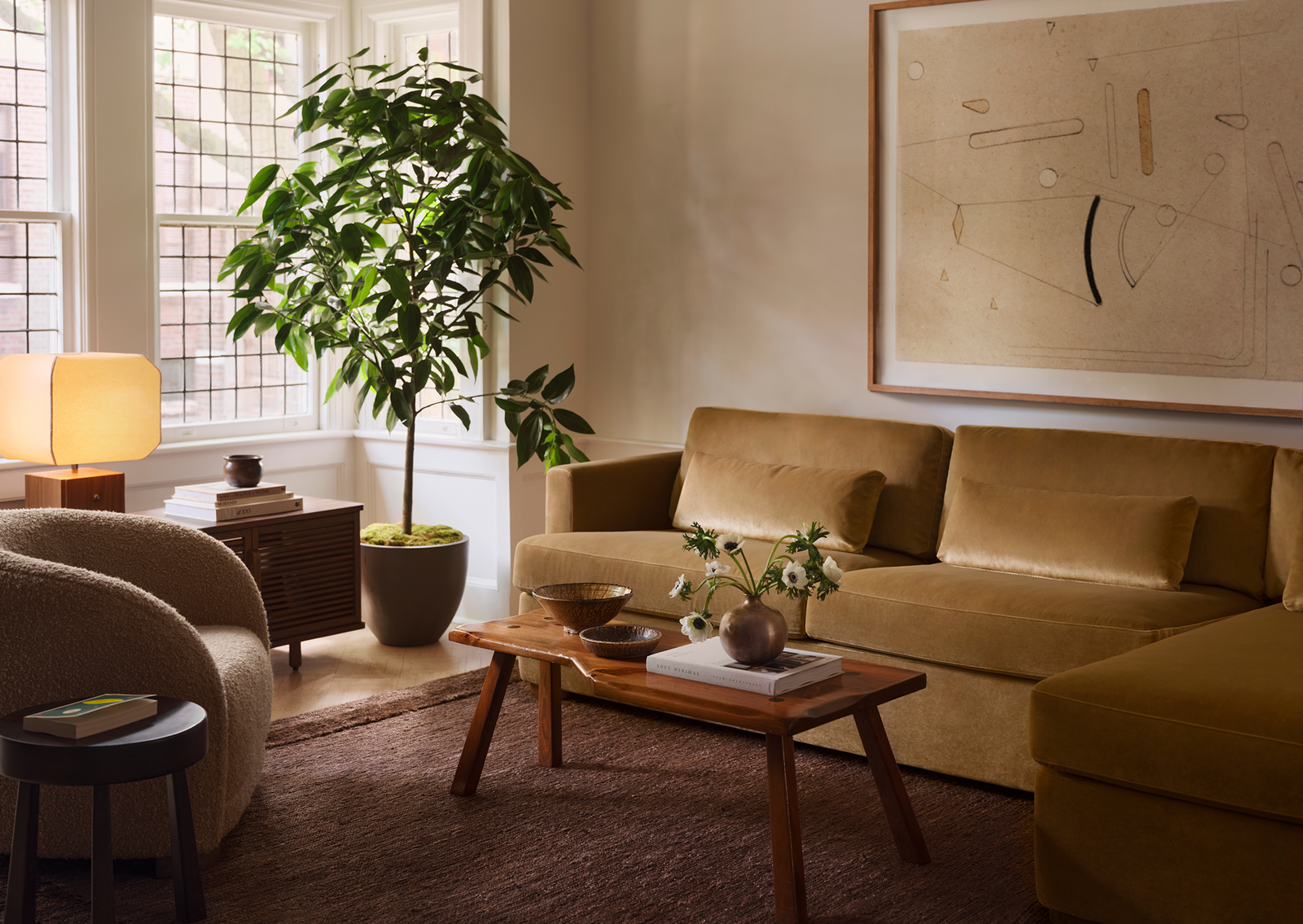 Living room with a gold velvet sofa, boucle swivel chair, and live-edge coffee table on a brown rug.