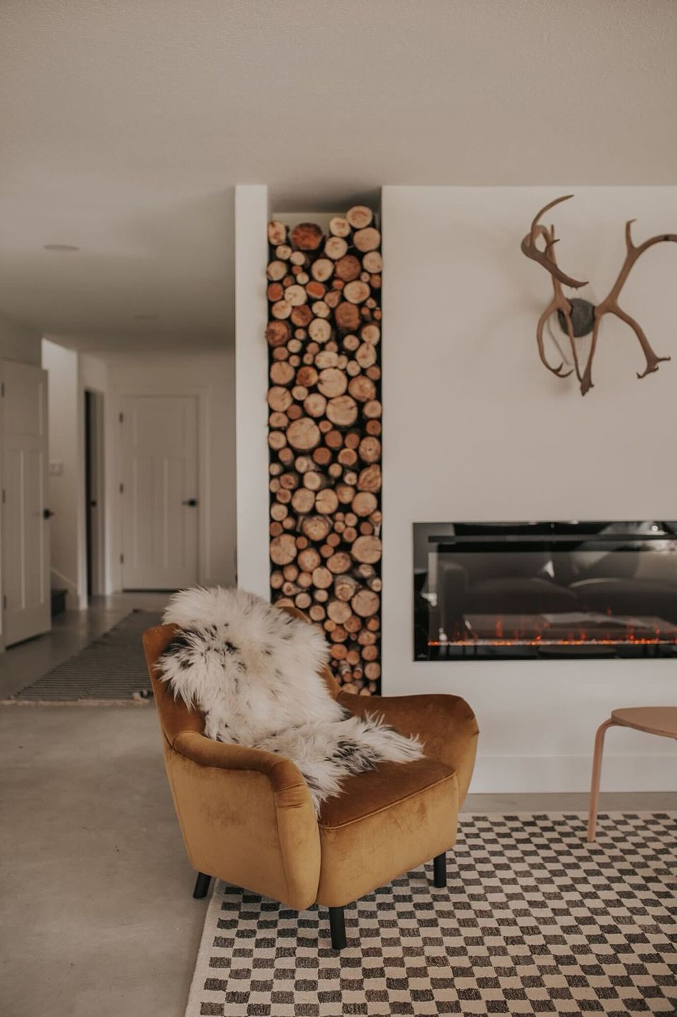 Contemporary minimalist fireplace with stacked wood storage and ochre velvet accent chair