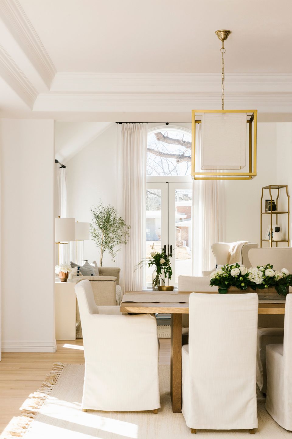 Serene neutral dining room with cream slipcover chairs, natural wood table, brass accents, and soft natural light from floor-to-ceiling windows