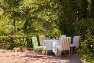 Tropical dining setup with verdant canopy, colorful upholstered chairs, and warm terracotta flooring evoking lush paradise.