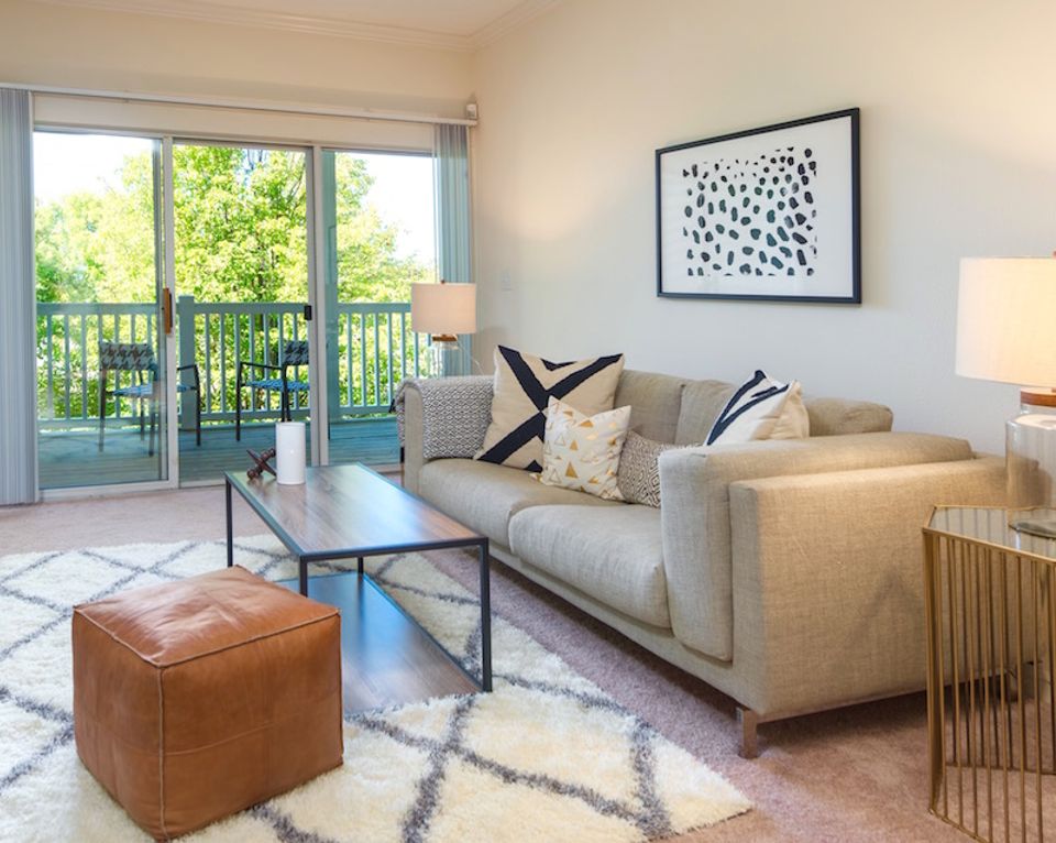 Bright airy living room with neutral sofa, cognac leather pouf, geometric rug, natural light, and coastal modern aesthetic.