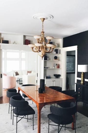 Contemporary dining room blending mid-century modern wood table with black chairs, brass chandelier, and navy accent wall against clean white shelving.