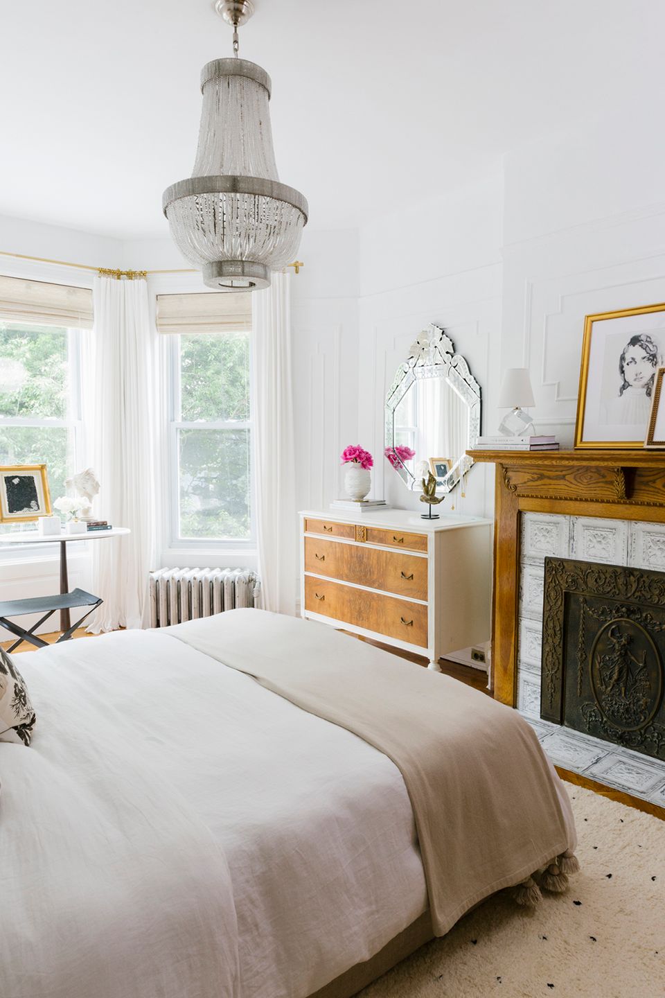 Elegant vintage-inspired bedroom with crystal chandelier, wood dresser, and fireplace accent