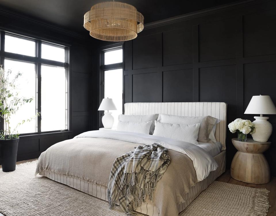 Modern bedroom with dark paneled walls, white bedding, and brass pendant light creating moody sophistication