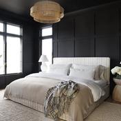 Modern bedroom with dark paneled walls, white bedding, and brass pendant light creating moody sophistication