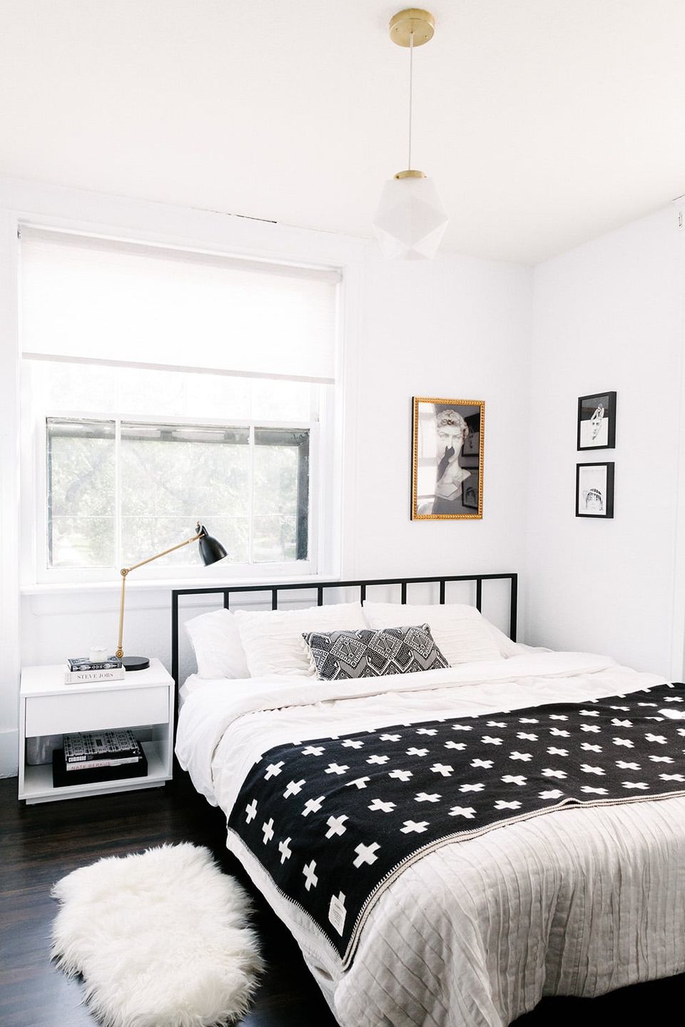 Minimalist mid-century bedroom with black spindle bed, white walls, black and white geometric bedding, and brass pendant light