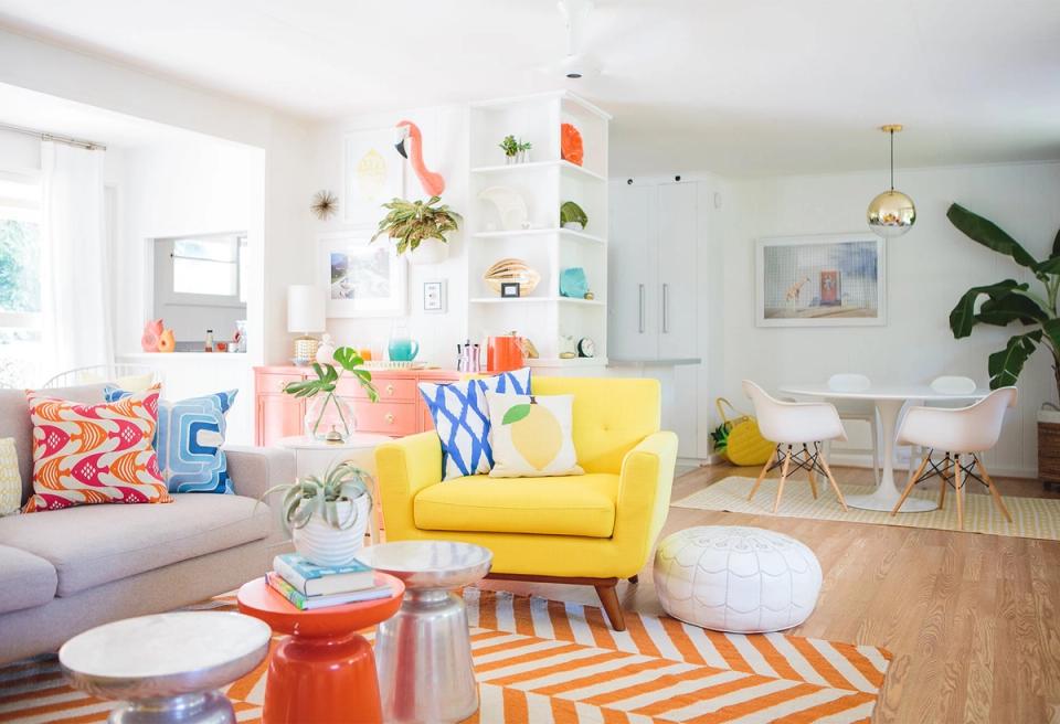 Bright eclectic living room with bold color blocking: yellow armchair, orange geometric rug, colorful pillows, and vibrant wall art creating playful, energetic modern aesthetic