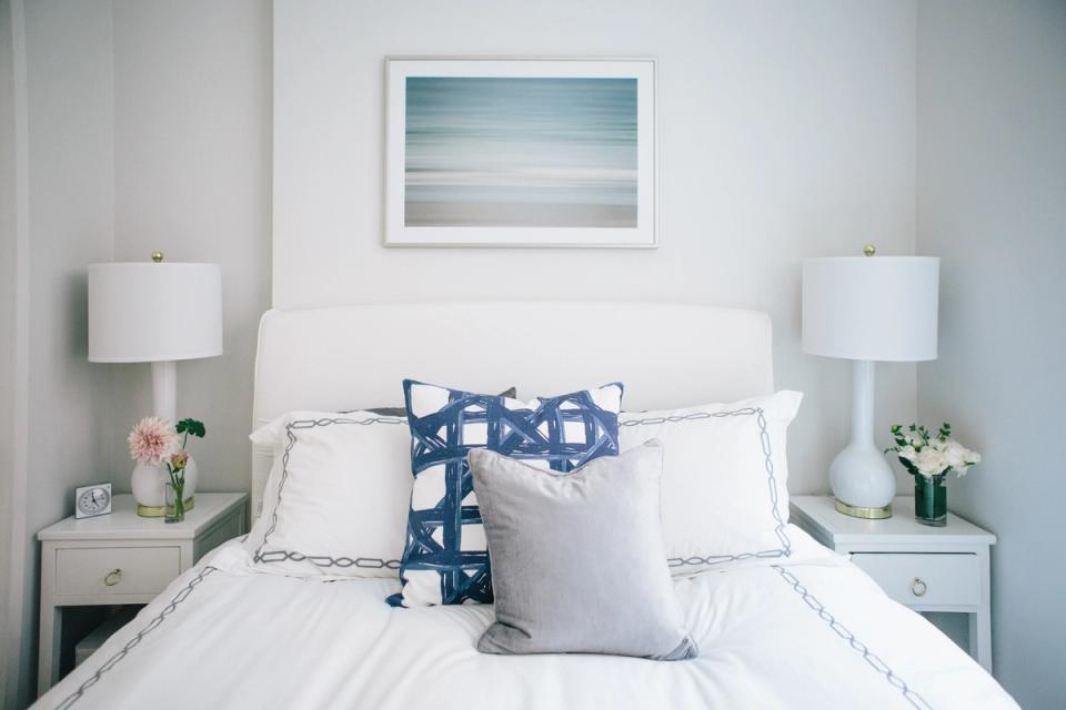Serene coastal bedroom with soft blue and white palette, minimalist decor, and calming landscape artwork above bed