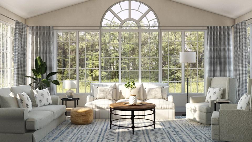 Bright sunroom with light gray seating, round black coffee table, and expansive arched windows framing green views