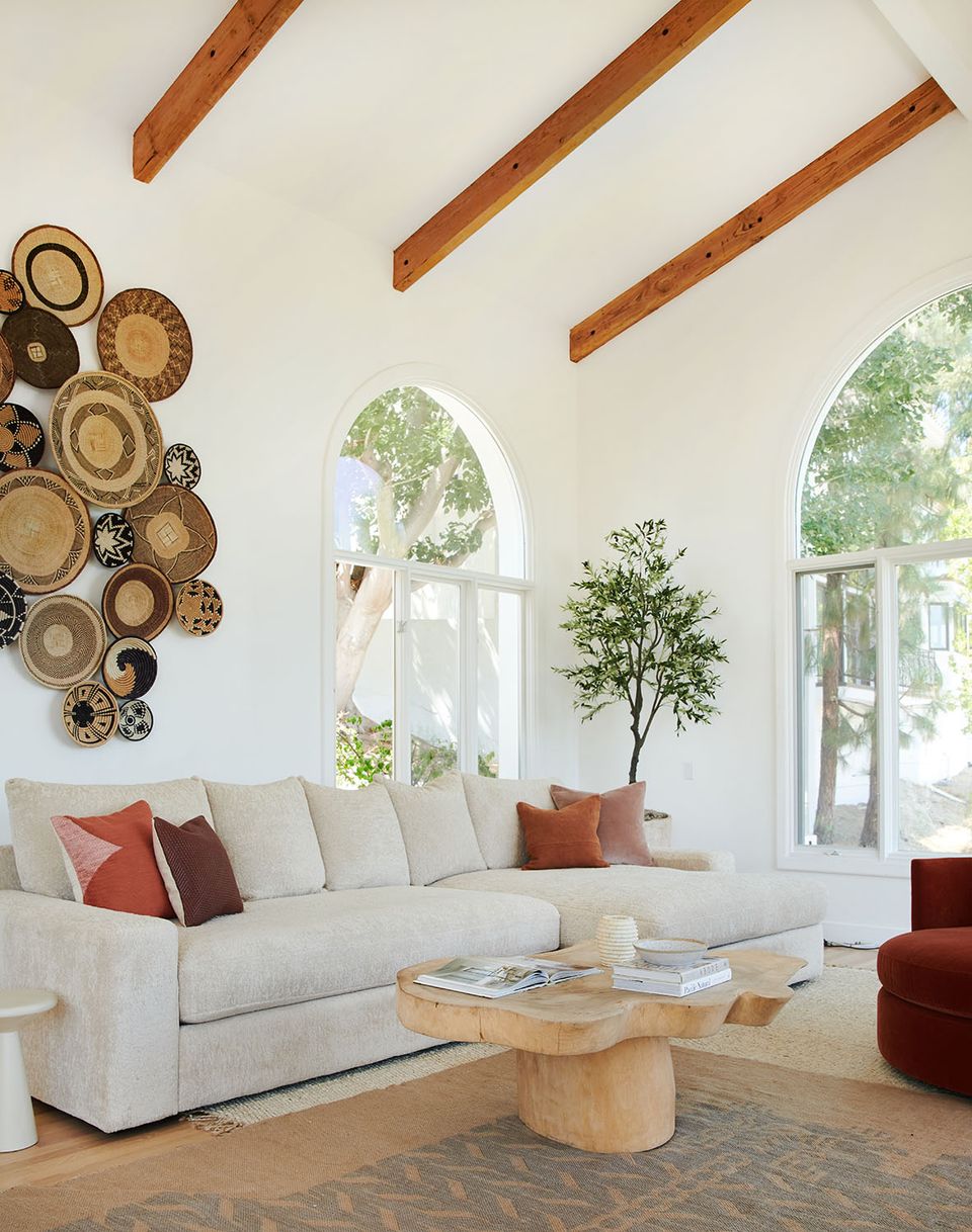 Organic modern living room with cream sofa, woven wall art, exposed wood beams, and warm accents.
