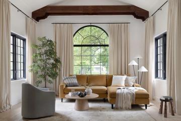 Warm English cottage living room with caramel sofa, cream linen, arched windows, and earthy 1970s-inspired tones