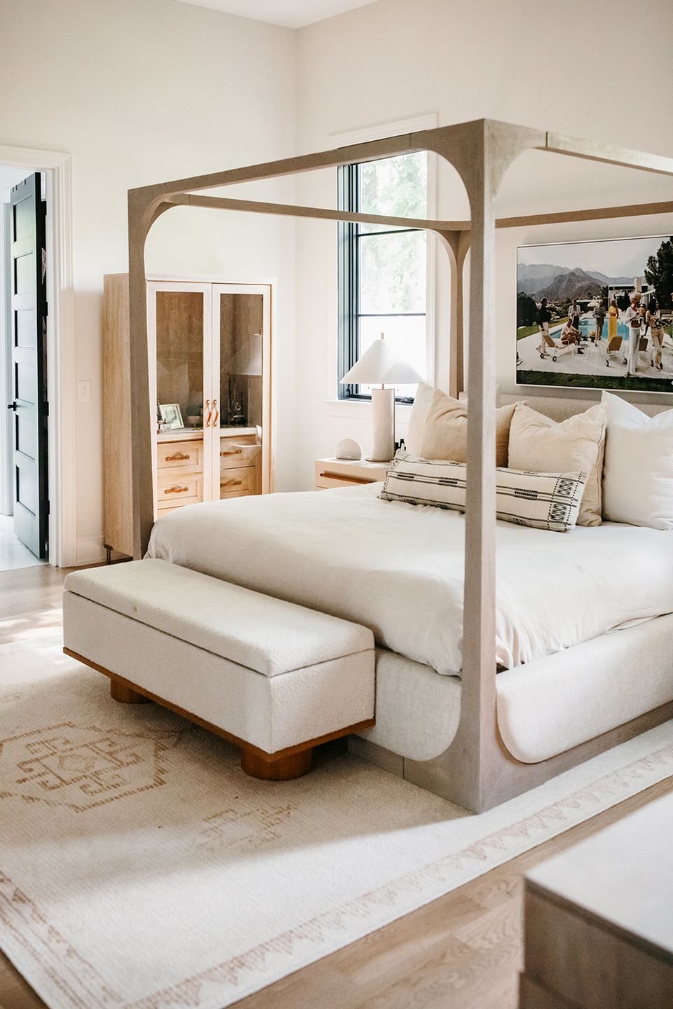 Light-filled boho bedroom with wood canopy bed, cream bedding, and earthy neutral tones